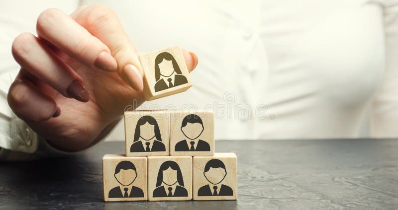 Business woman puts a wooden cube with the image of workers. Mixed staff concept. Personnel management in a team. Human resources. Dismissal employee. Hiring stock image