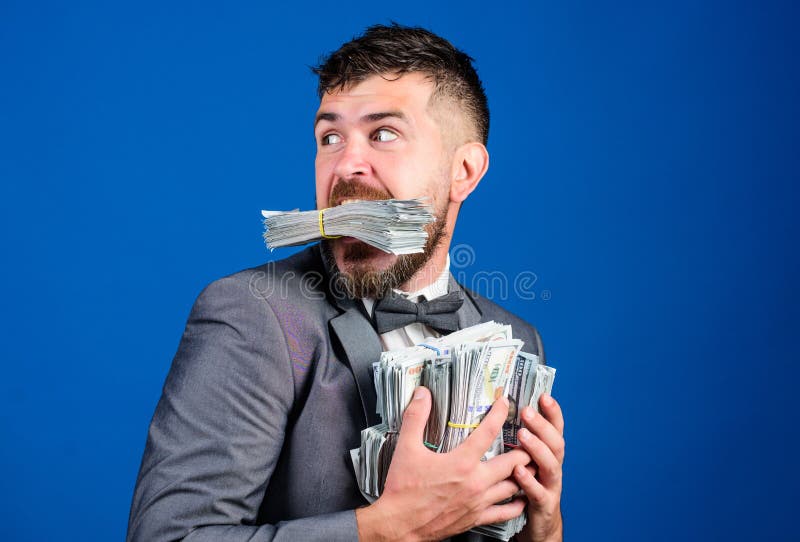 Steal money. Thief with piles dollars money. Earnings surprise concept. Man bearded businessman hold pile money blue. Background. Businessman surprised feels stock images